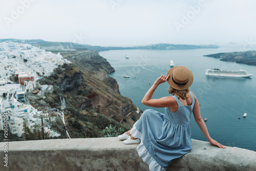 Travel Europe for summer holiday. Portrait of beautiful woman visitting old village Oia, Santorini island, Greece with sun hat and summer dress. photo