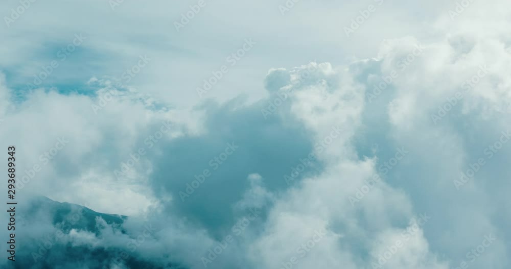 Aerial view flying in the midst of clouds in the sky with a mountain side in the background
