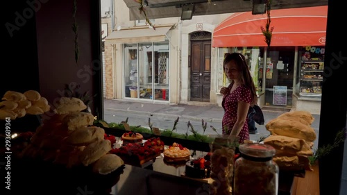 Beautiful girl in red dress is looking at confectionery shop window with very tasty and beautiful cakes outside. Indoor shooting