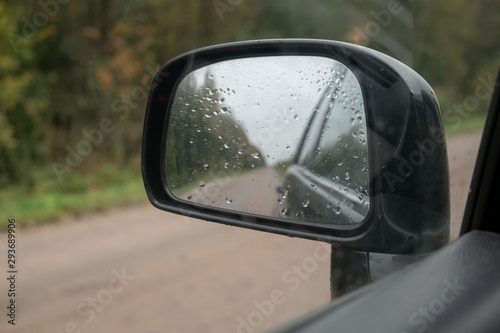 through a rearview mirror a dirt forest road is visible. Mirror covered with raindrops © Roman