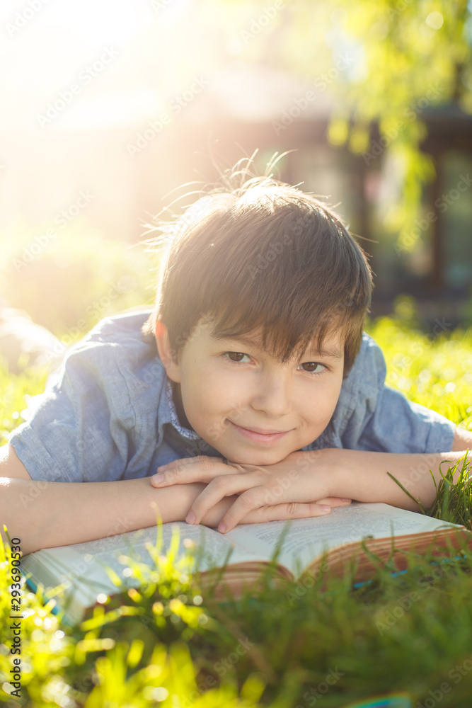 Cute smiling little boy lying on green grass in the park. Child reading the book outdoors. Dream, education and reading concept. Back to school! Happy time! Cute smiling little boy lying on green grass in the park. Child reading the book outdoors. Dream, education and reading concept. Back to school! Happy time!