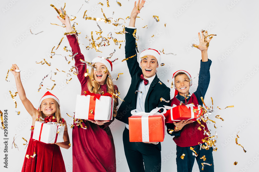 Young happy Christmas family with kids wearing Santa hats having fun with Christmas gifts in hand on white background