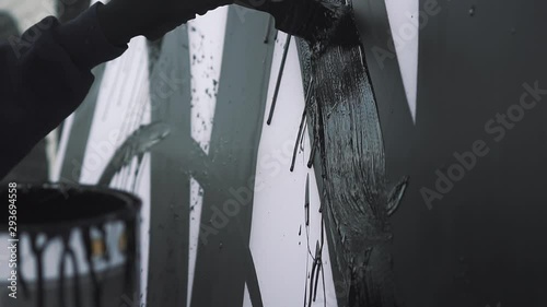 the artist paints with black paint on canvas, on the street. the paint drips slowly.