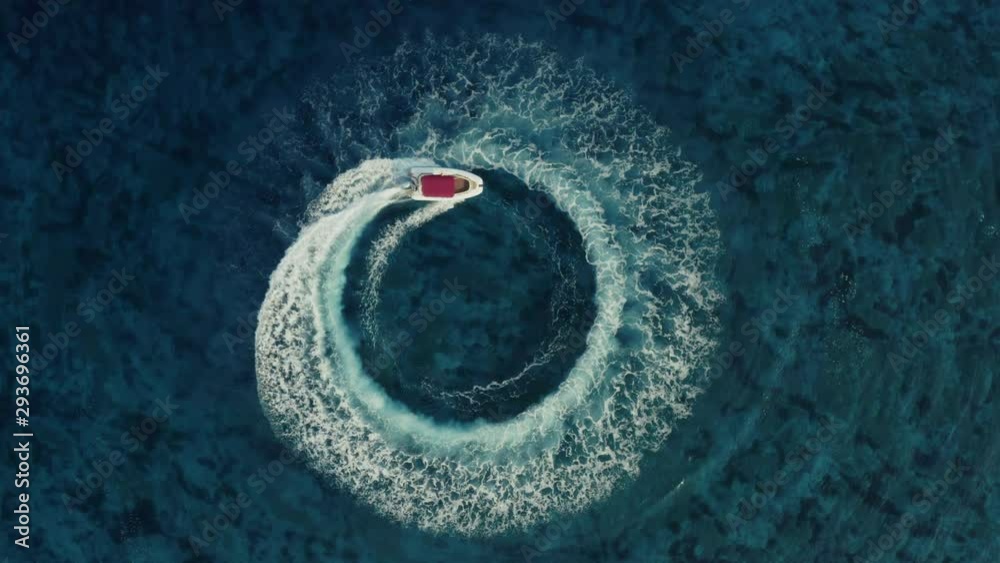 Slow motion aerial shot descending towards fast speedboat with a red roof top, going around in the circle and making beautiful shapes in the clear sea. Top travel destination. 4K.