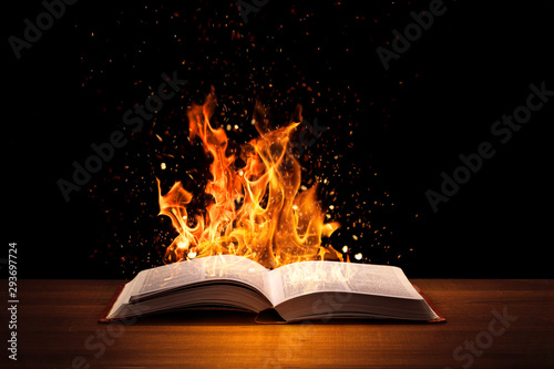 Holy Bible on fire on a wooded desk