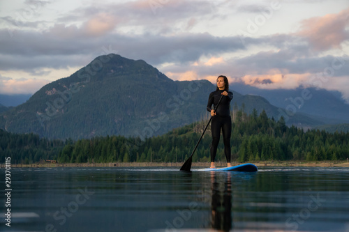 Adventurous Girl on a Paddle Board is paddling in a calm lake with mountains in the background during a colorful summer sunset. Taken in Stave Lake near Vancouver  BC  Canada.