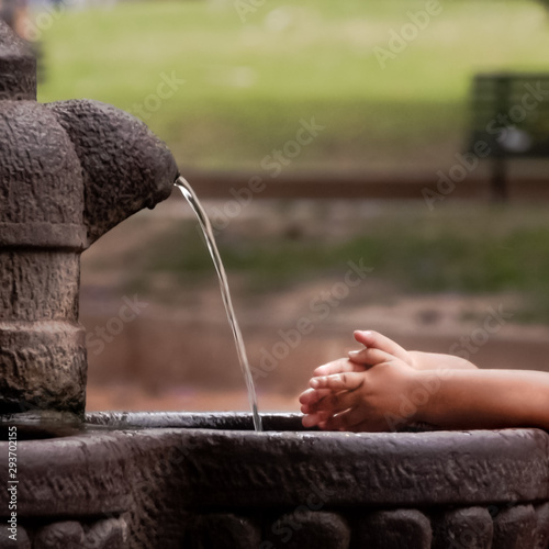 Manos de un niño lavándose las manos en una fuente en una plaza photo