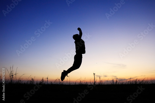 In the evening, a boy is jumping on the grassland