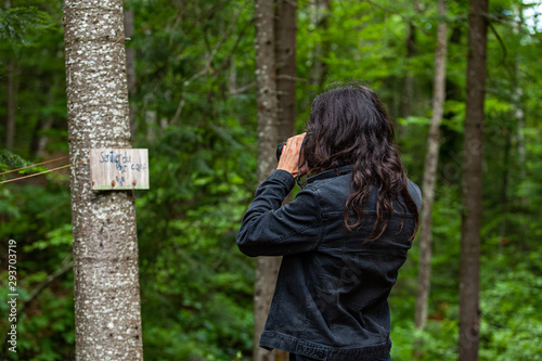 Diverse people enjoy spiritual gathering A professional male photographer with long black hair is seen in woodland wearing a black denim jacket as he photographs a spiritual sign on a tree.