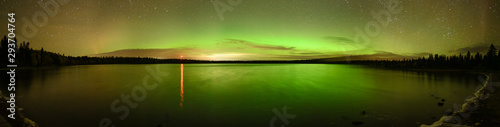 Bright green and orange Aurora (Northern Lights) , stars and clouds reflecting in a calm lake.