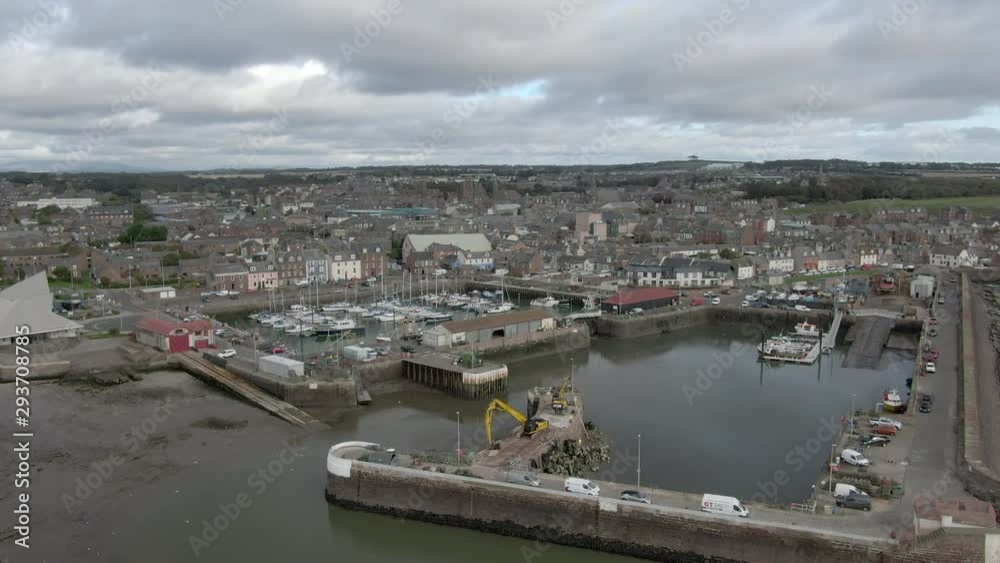An aerial view of Arbroath harbour and town on a cloudy day. Right to left circling view of the harbour with the town in the background. An aerial view of Arbroath harbour and town on a cloudy day. Right to left circling view of the harbour with the town in the background.
