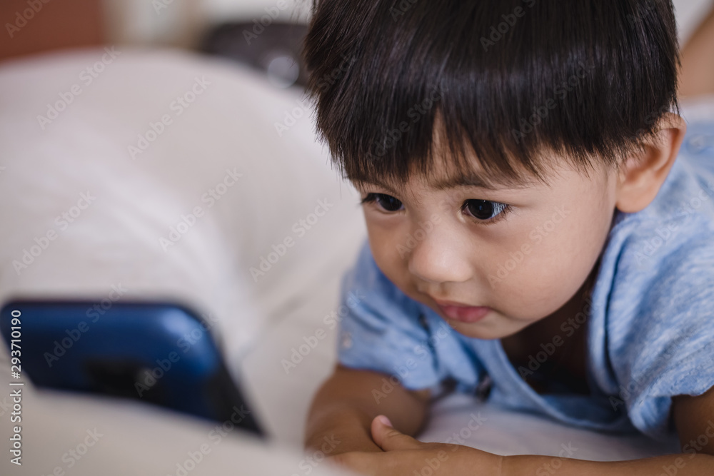 Asian child lying on bed and playing on mobile phone Asian child lying on bed and playing on mobile phone