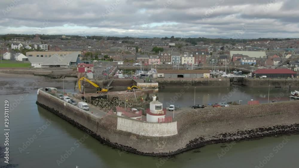 An aerial view of Arbroath harbour and town on a cloudy day. Right to left circling and descending view of the harbour with the town in the background. An aerial view of Arbroath harbour and town on a cloudy day. Right to left circling and descending view of the harbour with the town in the background.