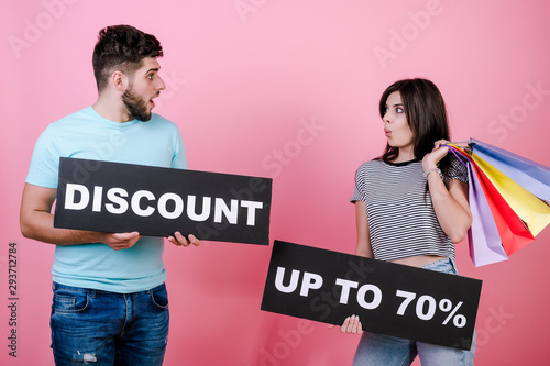 happy smiling handsome couple man and woman with discount up to 70% sign and colorful shopping bags isolated over pink