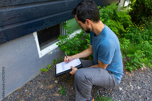 Indoor damp & air quality (IAQ) testing. A close up view on environmental home quality inspector at work, filling in a form as he inspects the exterior of a cellar window, with room for copy. photo