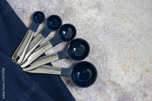 metal measuring spoons with dark blue bowl and dark blue napkin on a marble countertop background for cooking or baking concepts