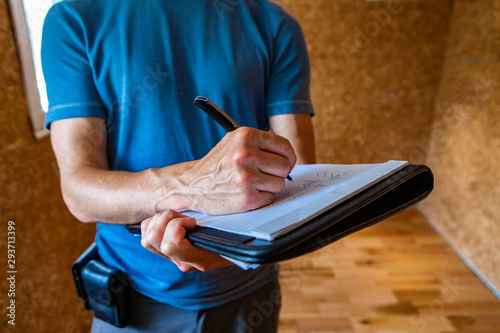 Indoor damp & air quality (IAQ) testing. A close-up and front view of a professional male home inspector, using a blue pen to take notes on paper during an inspection of a domestic property. photo