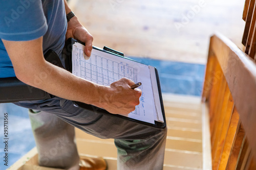 Indoor damp & air quality (IAQ) testing. A close up and high angle view of a professional male wearing blue t-shirt, writing out forms during a home inspection, standing on stairs with copy-space.