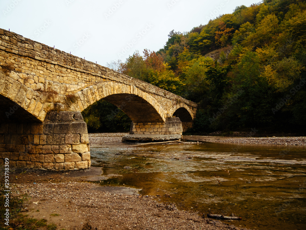 Old stone bridge. Autumn trees in the mountains. Mountain river