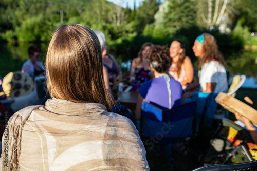 Sacred drums during spiritual singing. A close-up view on the back of a blonde woman's head as she watches a circle of people singing and playing traditional native music in a park with copy-space.