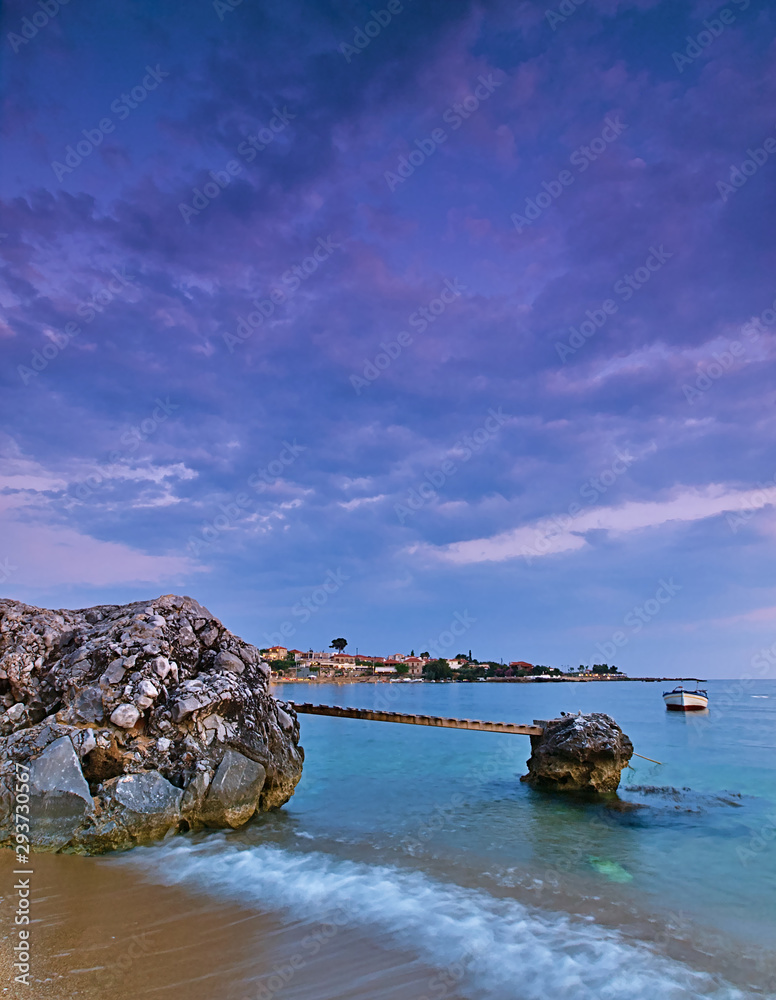 Beautiful sandy beach with rocks in the sea, small bridge and  boat at dusk time, Stoupa, Peloponnese, Greece.