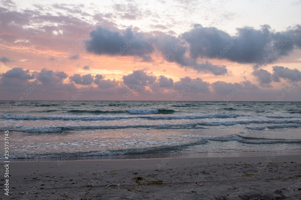 Dawn on the Mediterranean coast, Tunisia Sand in the foreground, small waves, the sun above the horizon, long clouds