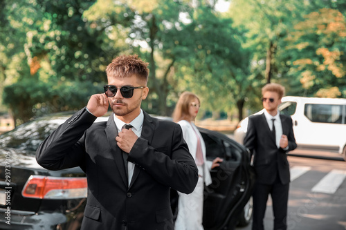 Young celebrity with bodyguards near car outdoors photo