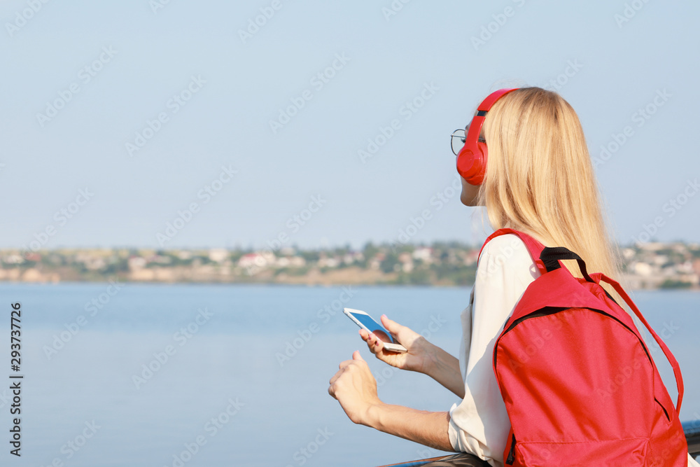 Beautiful young woman listening to music near river
