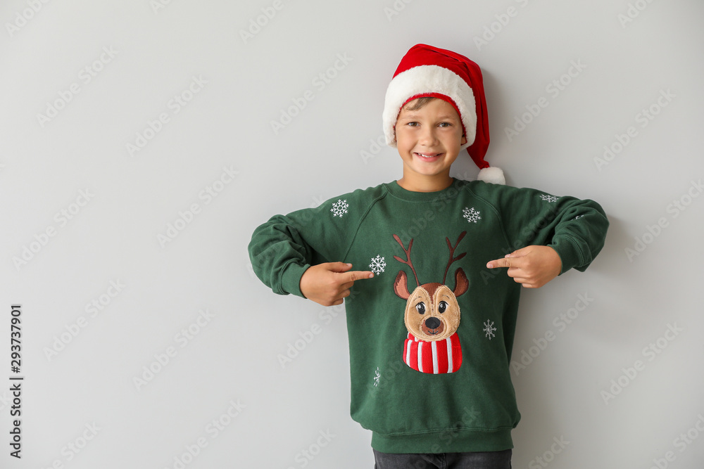 Funny boy in Christmas sweater and Santa hat on light background