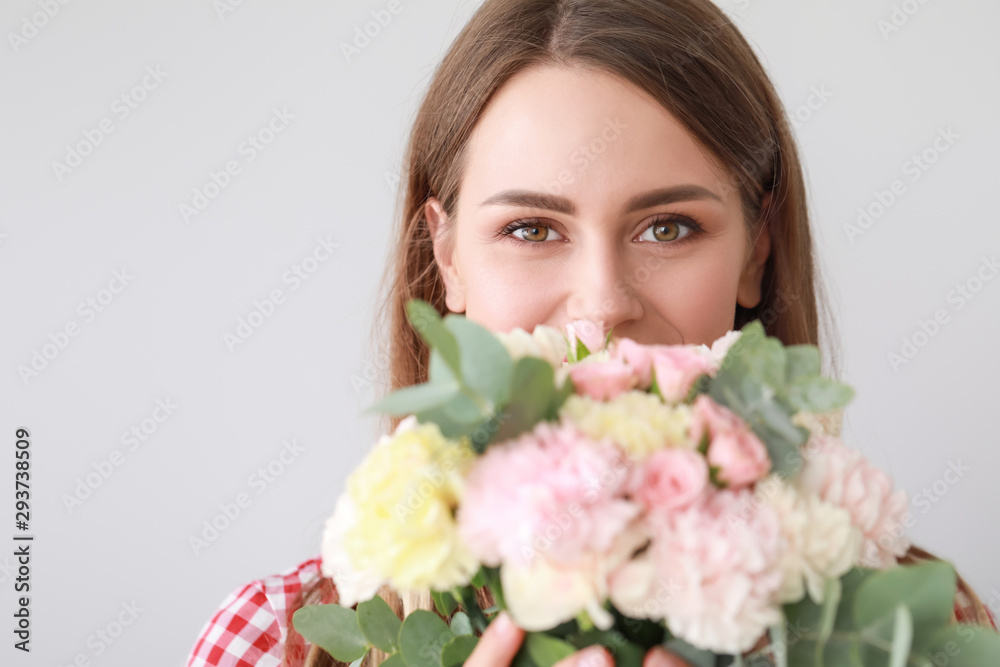 Beautiful young woman with bouquet of carnation flowers on light background