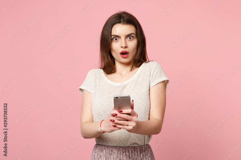 Shocked young woman in casual light clothes posing isolated on pastel pink wall background. People lifestyle concept. Mock up copy space. Keeping mouth open, using mobile phone, typing sms message. Shocked young woman in casual light clothes posing isolated on pastel pink wall background. People lifestyle concept. Mock up copy space. Keeping mouth open, using mobile phone, typing sms message.