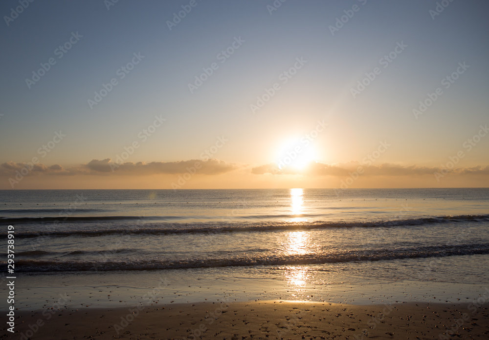 Dawn on the Mediterranean coast, Tunisia Sand in the foreground, small waves, the sun above the horizon, long clouds