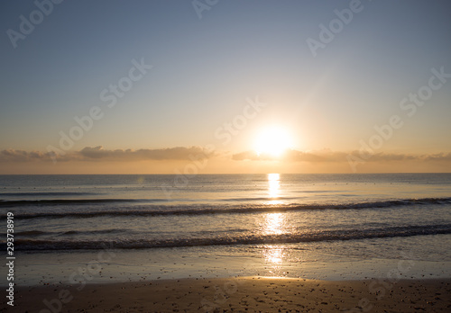Dawn on the Mediterranean coast  Tunisia Sand in the foreground  small waves  the sun above the horizon  long clouds