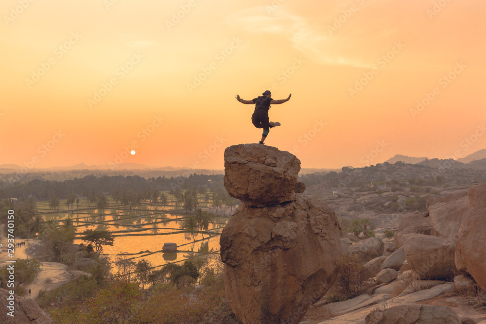 An Acrobat performs acrobatics at the spectacular sunset point at Hampi in Karnataka, India. Acro yoga , bouldering and music performers enjoy daily sunset here. Gymnasts outdoor