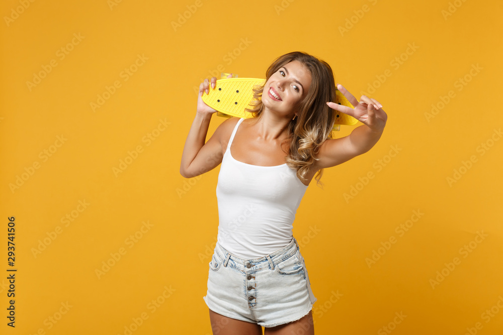Pretty young woman girl in light casual clothes posing isolated on yellow orange background, studio portrait. People lifestyle concept. Mock up copy space. Holding skateboard, showing victory sign. Pretty young woman girl in light casual clothes posing isolated on yellow orange background, studio portrait. People lifestyle concept. Mock up copy space. Holding skateboard, showing victory sign.