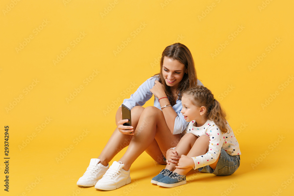 Woman using mobile phone have fun with cute child baby girl 4-5 years old. Mommy little kid daughter isolated on yellow background studio portrait Mother's Day love family parenthood childhood concept Woman using mobile phone have fun with cute child baby girl 4-5 years old. Mommy little kid daughter isolated on yellow background studio portrait Mother's Day love family parenthood childhood concept