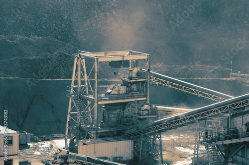 Machinery at a quarry with piles of sand and aggregate in the background. With colour toning