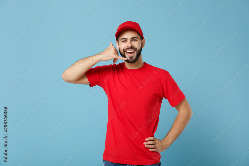 Delivery man in red uniform workwear isolated on blue wall background, studio portrait. Professional male employee in cap t-shirt print working as courier dealer. Service concept. Mock up copy space.