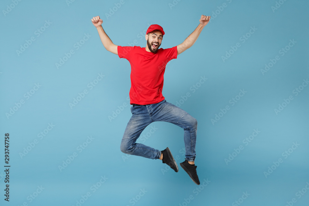 Delivery man in red uniform workwear isolated on blue wall background, studio portrait. Professional male employee in cap t-shirt print working as courier dealer. Service concept. Mock up copy space. Delivery man in red uniform workwear isolated on blue wall background, studio portrait. Professional male employee in cap t-shirt print working as courier dealer. Service concept. Mock up copy space.