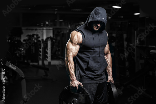Muscular athletic bodybuilder fitness model posing after exercises in gym