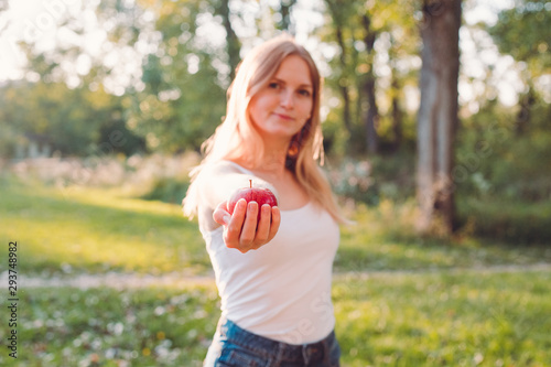 Woman holding fresh red apple on the blur nature background. Lunch in the park. Healthy, organic food concept. Harvest of fruits