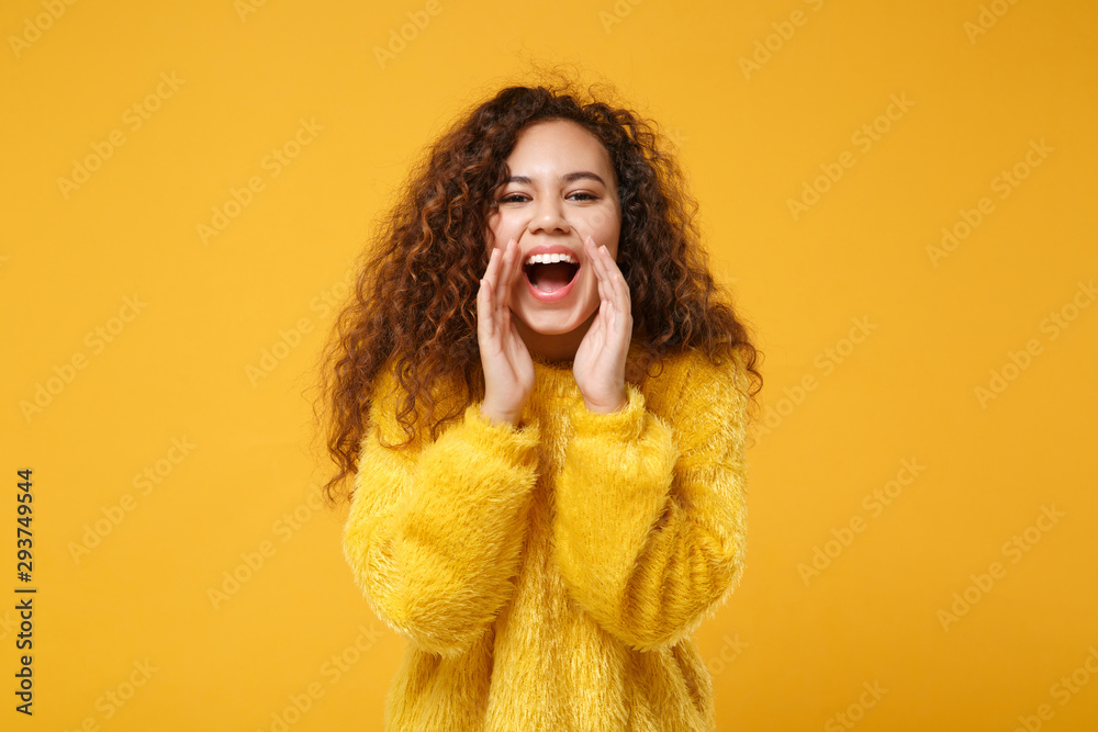 Cheerful young african american girl in fur sweater posing isolated on yellow orange wall background, studio portrait. People lifestyle concept. Mock up copy space. Screaming with hands near mouth. Cheerful young african american girl in fur sweater posing isolated on yellow orange wall background, studio portrait. People lifestyle concept. Mock up copy space. Screaming with hands near mouth.