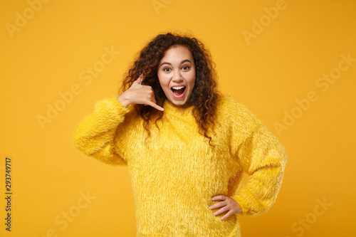 Excited young african american girl in sweater posing isolated on yellow orange background. People lifestyle concept. Mock up copy space. Keeping mouth open doing phone gesture like says call me back. © ViDi Studio