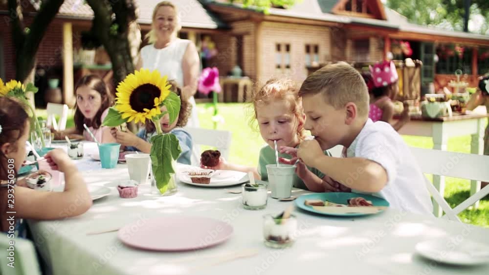 Small children sitting at the table outdoors on garden party in summer, eating. Small children sitting at the table outdoors on garden party in summer, eating.