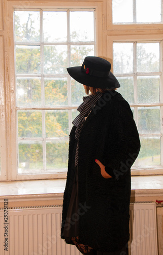 a lonely woman in a black hat looks out of a large bright window