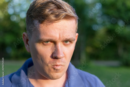 Man with a scornful disdainful disrespectful look. Portrait of a young guy on nature background, feelings and people reaction. Anger rage and hatred photo