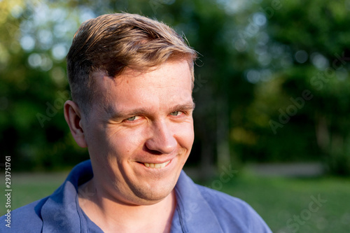 Portrait of a young man on nature background. Emotion facial expression. Smug smile, feelings and people reaction.