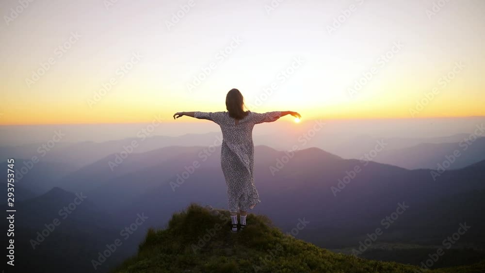 Young beautiful woman in a long dress developing in the wind at the top of the mountain at sunset Young beautiful woman in a long dress developing in the wind at the top of the mountain at sunset