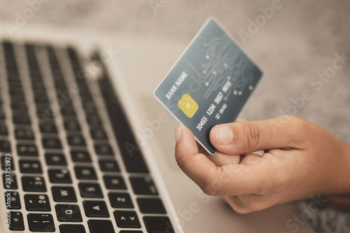 Hand holding a credit card next to a laptop