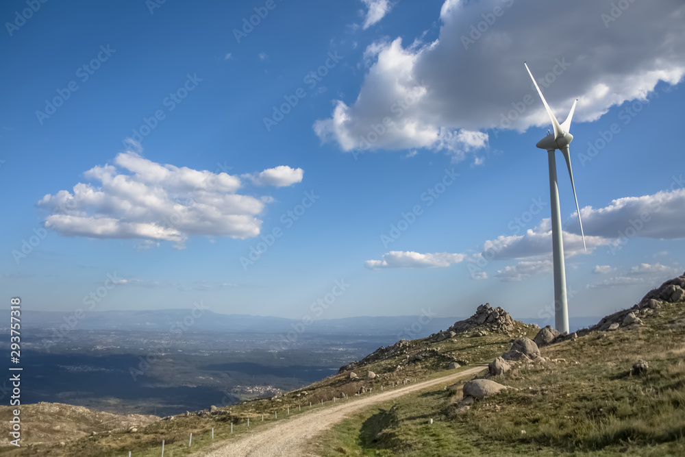 View of a wind turbine on top of mountains, blue sky as background View of a wind turbine on top of mountains, blue sky as background